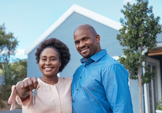 A Ghanaian couple smiles in front of their new home, protected by the Mortgage Protection Plan. A happy couple stand in front of their new home, holding the house keys.