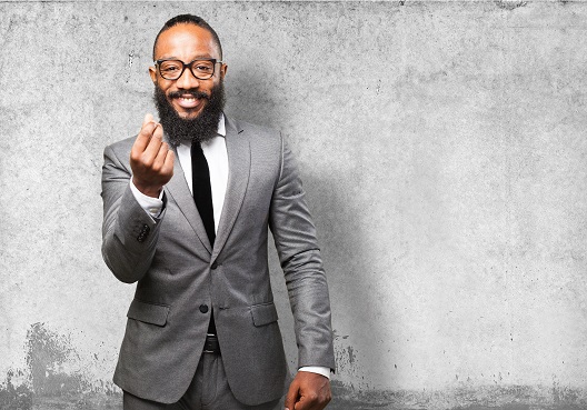 A man wearing a grey suit prepares to deliver a presentation about the Prestige Pension Scheme. A Ghanaian man dressed in a suit and tie prepares to speak about a pension plan for a company.