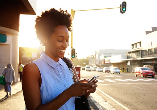 A woman standing on a busy sidewalk searches online for an office address for Old Mutual Ghana.