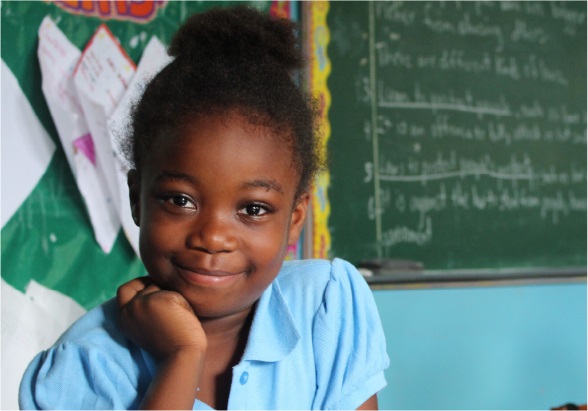 A young girl in a classroom sits in front of a blackboard and smiles A schoolgirl smiles in a photo taken at her school.