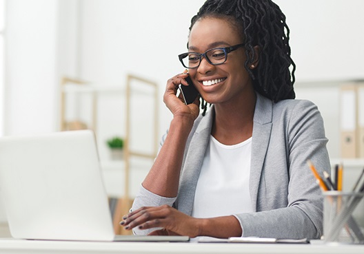 A financial adviser sits at her desk in front of her laptop and talks to a client on the phone.