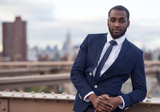 A financial adviser who gives clients advice on insurance policies outside his office. A financial adviser wearing a dark blue suit stands outside of his office.