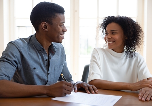 A man and woman sitting alongside each other smiling at one another